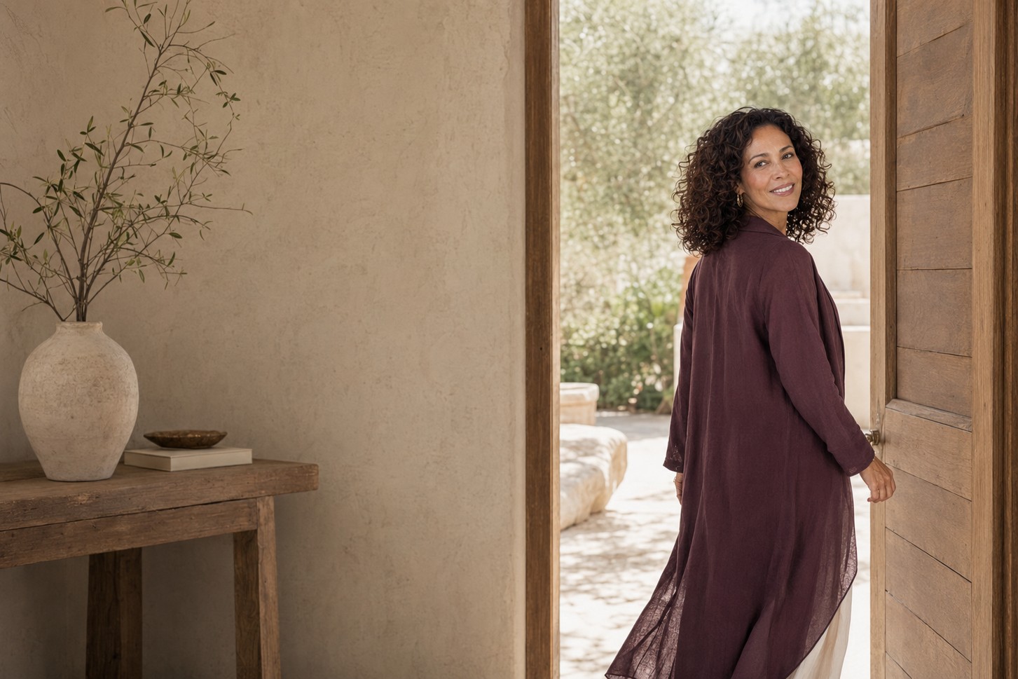 A woman pauses at an open doorway and looks back before stepping into the light